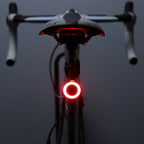 A bright circular red LED bicycle taillight mounted on a seat post against a dark background.