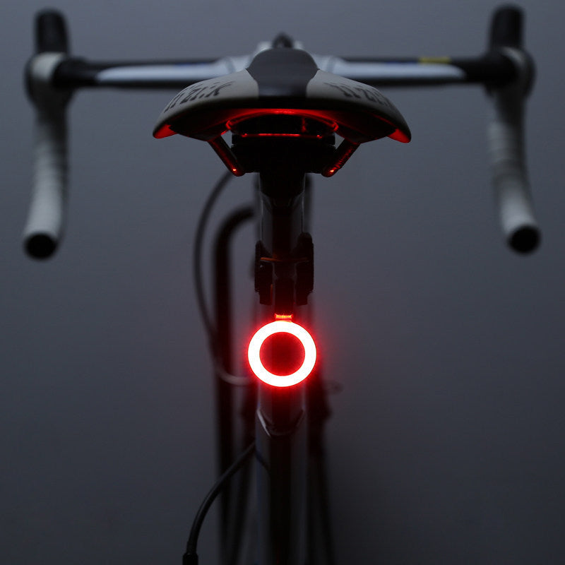A glowing red circular LED bicycle taillight mounted on a bike seat post, viewed from behind in low light.
