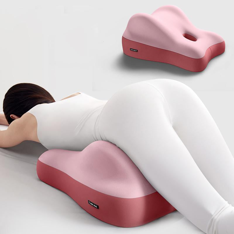 A pink, ergonomic, two-tone foam cushion used to elevate the hips for face-down reclining and comfort.