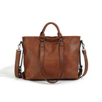 Large brown soft leather tote bag with top handles, detachable shoulder strap, and dark hardware on white background.