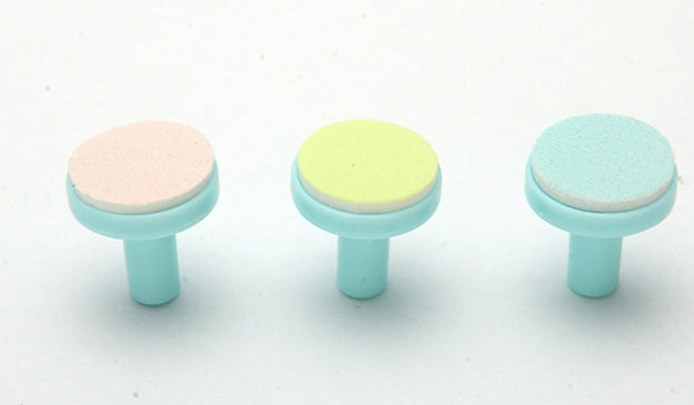 Three replacement nail trimmer heads with light blue plastic bases and textured pads in pink, yellow, and blue.