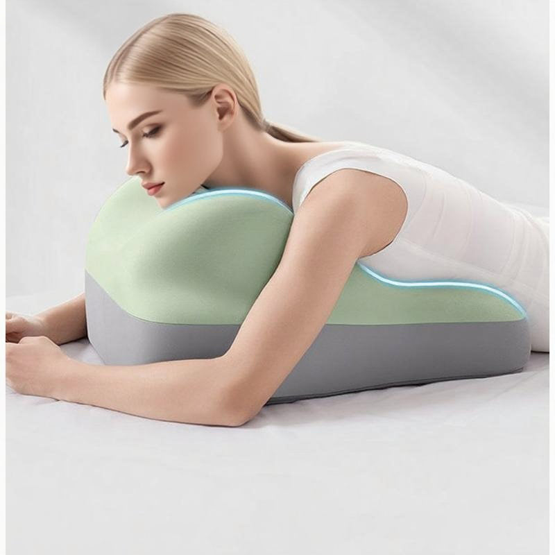 A woman rests chest-down on a contoured, two-toned mint green and grey foam support cushion on a white bed.