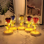 Five glittery roses in varied colors encased in glass domes on wooden bases, illuminated by warm LED fairy lights.