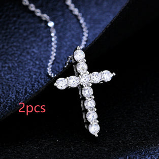 Silver tone chain necklace with a cross pendant set with sparkling round clear stones on a black background.