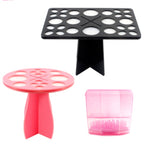 Black and pink plastic makeup brush drying racks and holders with multiple sized circular slots for tools.