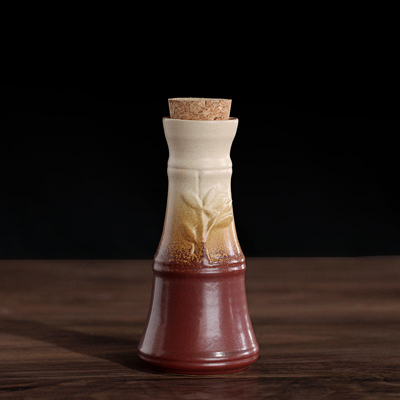 Ceramic wine decanter with a cork stopper, featuring a gradient finish from dark red to cream and embossed leaf design.
