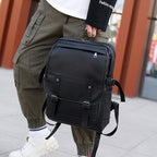 A black leather retro-style backpack with buckled front straps, front zip pocket, and side adjustable gear straps.