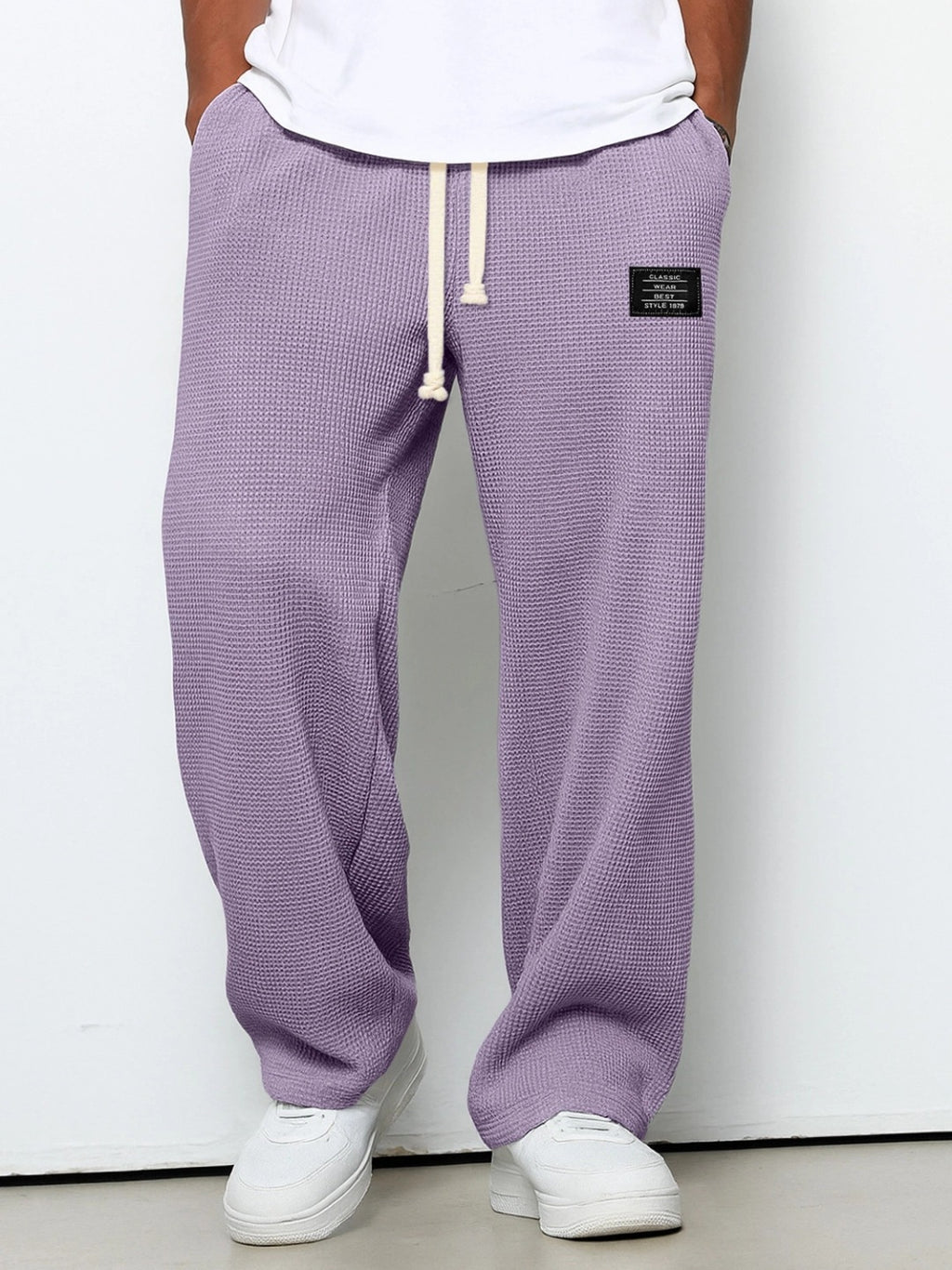 Loose, lavender-colored men’s waffle-knit straight pants with a white drawstring waist and a small black logo patch.