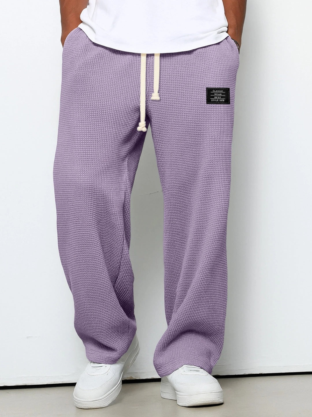 Loose, lavender-colored men’s waffle-knit straight pants with a white drawstring waist and a small black logo patch.