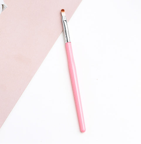 A makeup brush with a bright pink handle, silver ferrule, and soft brown synthetic bristles on a pink and white surface.