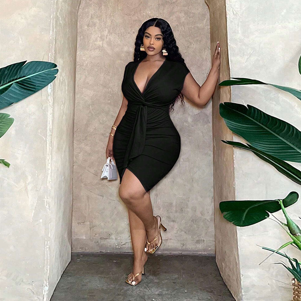 Model in a black V-neck, waist-tie, ruched hip-skimming dress with short sleeves, posing in an arched entryway.
