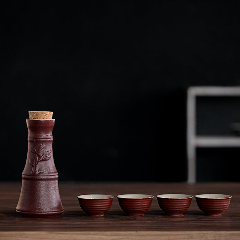 A brown, rustic ceramic sake set with a cork-topped decanter and four ribbed cups on a wooden table.