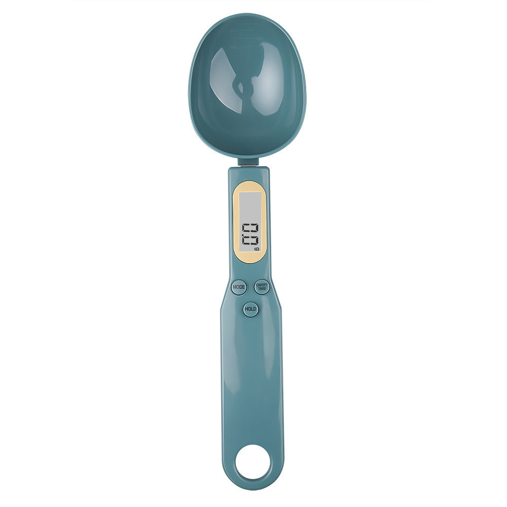 Blue plastic digital spoon scale with an LCD display showing "0.0g," mode, tare, and hold buttons on the handle.