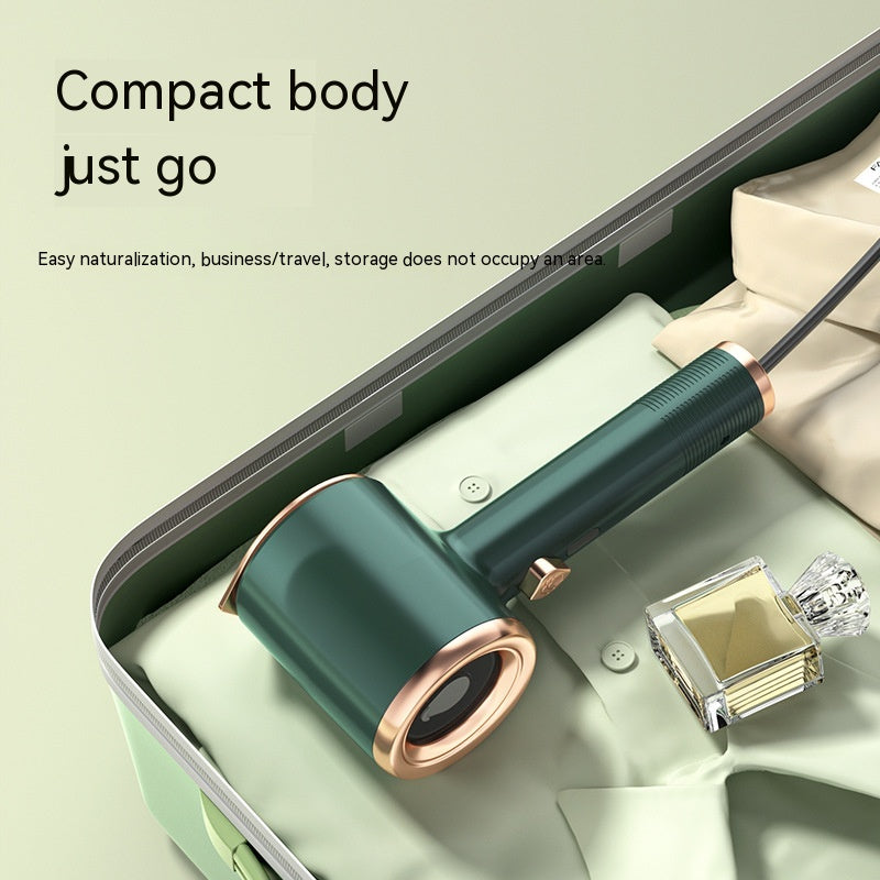Compact dark green and gold handheld garment steamer placed inside a suitcase with clothing and perfume.