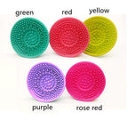 Five colorful, silicone circular makeup brush cleaning pads with textured surfaces, labeled by color on a white background.