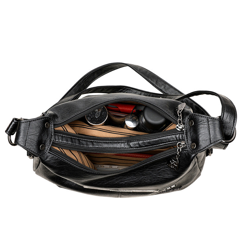 Top-down view of an open black soft leather shoulder bag with multiple zippered compartments and tan striped lining.