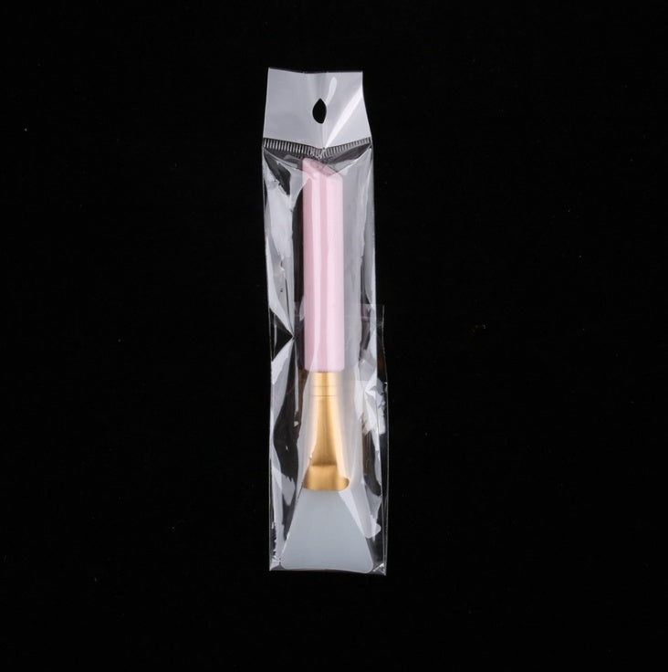 A pink and gold silicone mask brush for beauty applications, sealed in a clear plastic protective packaging.