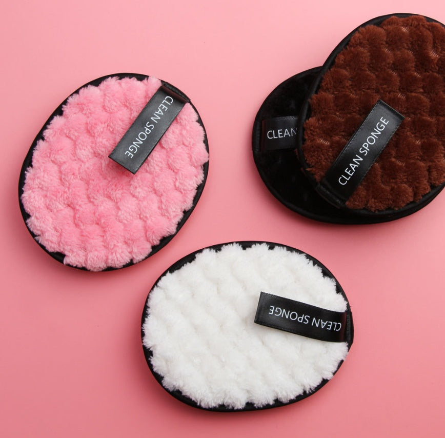 Three fuzzy, round cleansing sponges in pink, brown, and white with black trim and "CLEAN SPONGE" labels on a pink background.