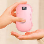 A person holds a smooth, pink, pebble-shaped electric hand warmer with a digital display showing "60" degrees.