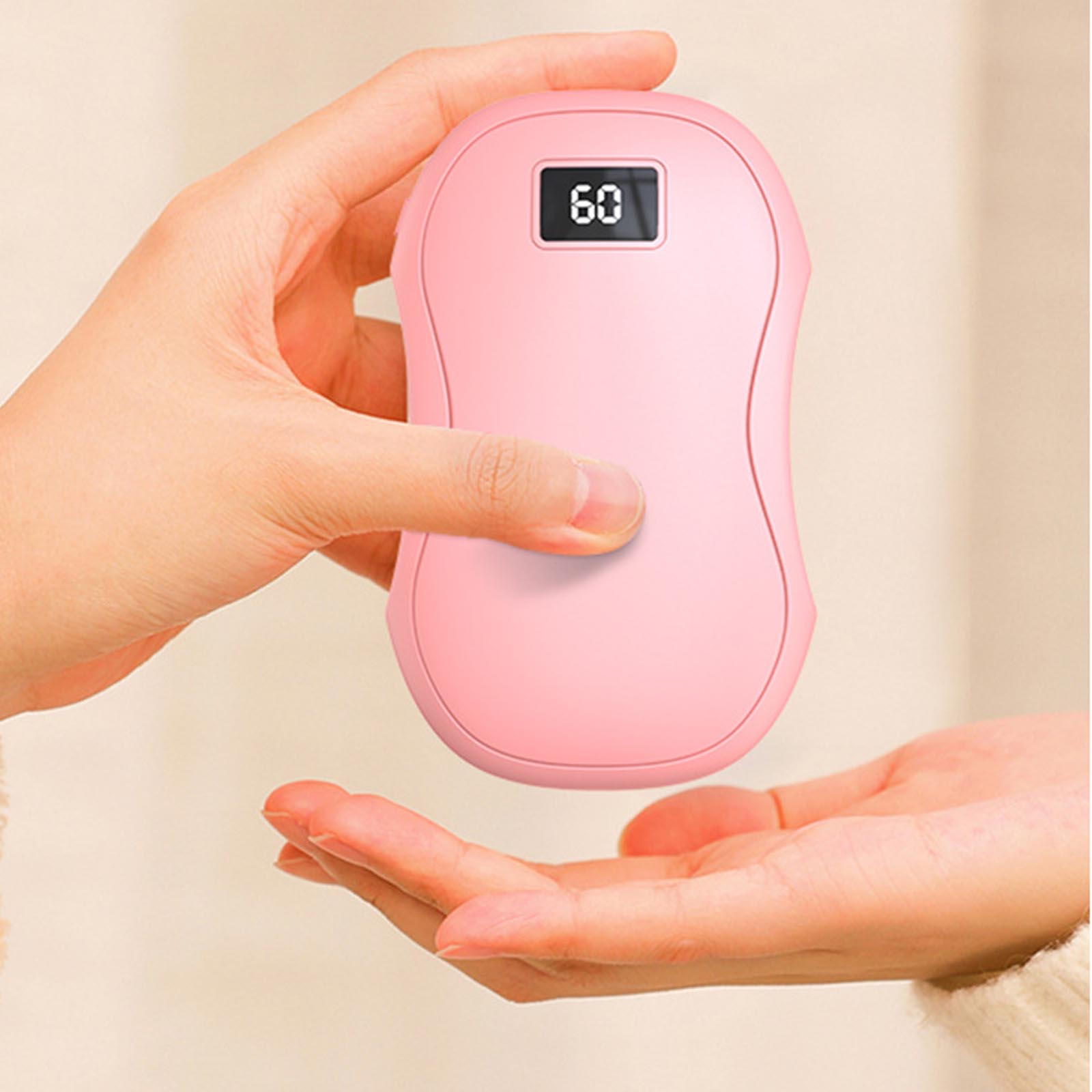 A person holds a smooth, pink, pebble-shaped electric hand warmer with a digital display showing "60" degrees.