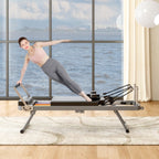 Woman doing pilates on a sleek, black foldable reformer machine with a metal frame in a bright room overlooking water.