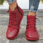 Women's red, flat ankle boots featuring side zippers, lace-up fronts, and a smooth, faux leather finish.