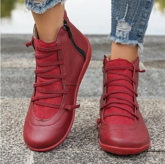 Women's red, flat ankle boots featuring side zippers, lace-up fronts, and a smooth, faux leather finish.