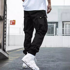 Black cargo joggers with large side pockets and ribbed cuffs, styled with white sneakers in an urban setting.