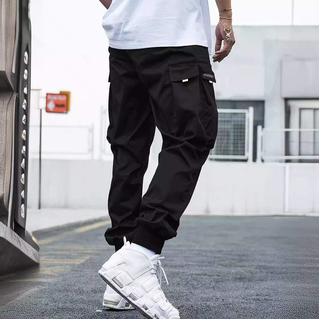 Black cargo joggers with large side pockets and ribbed cuffs, styled with white sneakers in an urban setting.