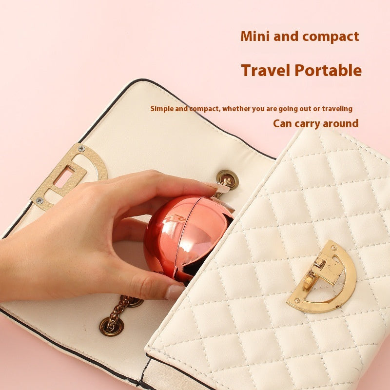 A hand places a metallic rose-gold, spherical reusable lint roller into a quilted cream-colored handbag.