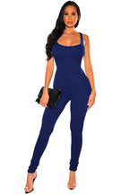 A woman wearing a royal blue, sleeveless, form-fitting stretch jumpsuit with a scoop neck, holding a black clutch.
