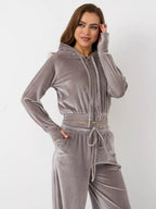 A woman wearing a grey velour two-piece set: a cropped zip-up hoodie and matching drawstring high-waisted joggers.