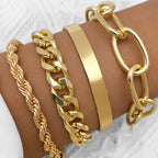 A set of four gold-toned hip hop bracelets on a wrist, featuring rope, cuban link, smooth cuff, and oval link chains.