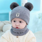 Baby wearing a gray wool hat with two fuzzy pom-poms, a "15" patch, and a matching "love me more" neck warmer.
