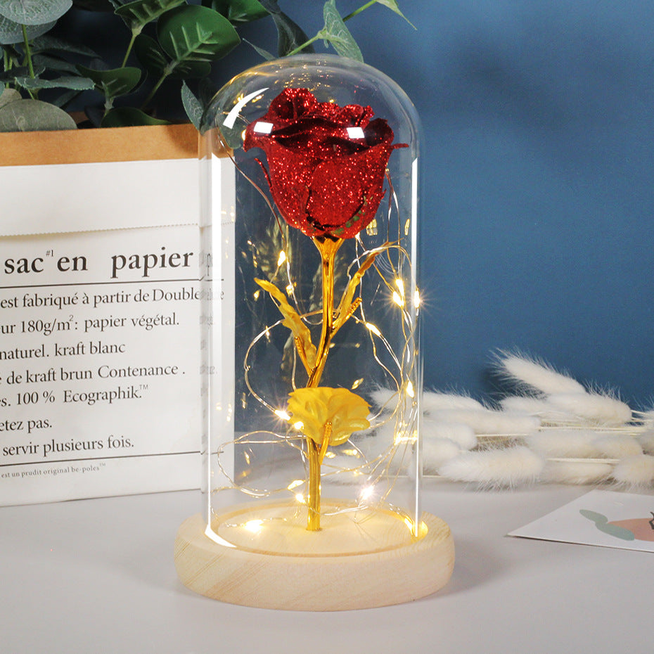 Sparkling red glitter rose in a glass dome on a wooden base with warm LED fairy lights, perfect for Valentine's Day.