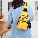Bright yellow canvas sling backpack with black trim, multiple pockets, and a USB port worn over a light blue shirt.