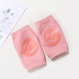 Pair of soft pink terry cloth baby knee pads featuring non-slip orange smiley face silicone grippers.
