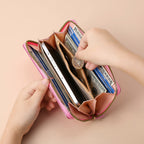 An open pink multi-functional clutch purse holding a smartphone, cards, cash, and coins on a light peach background.