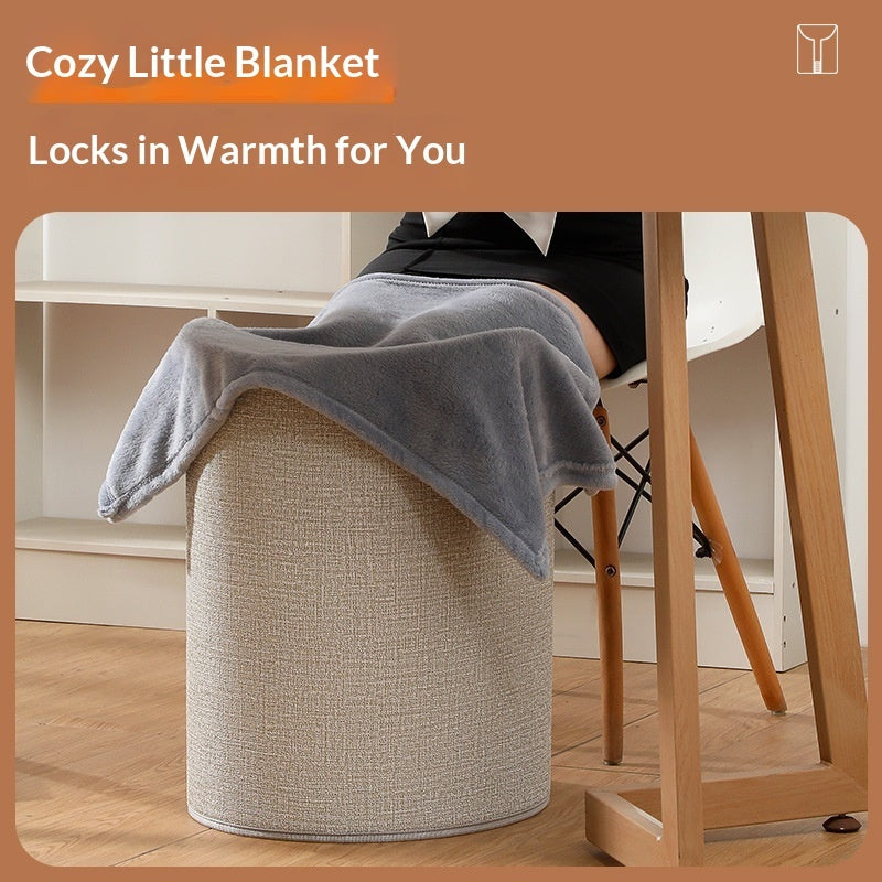 Grey plush foot warmer blanket draped over a textured beige cylindrical office stool under a desk.