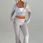 A woman wears a beige knit two-piece set: a cropped zip-up hoodie and matching low-rise flared pants.