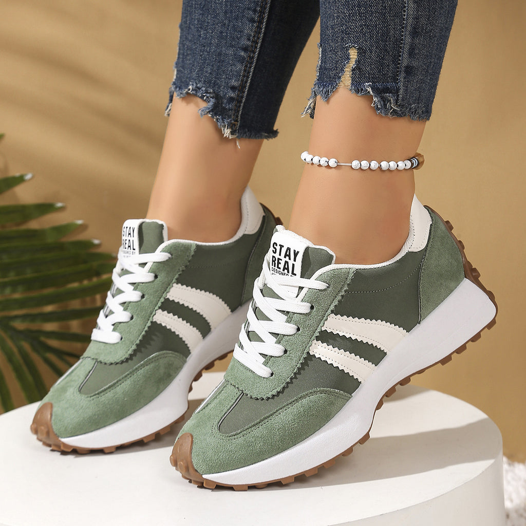 Green and white suede-look lace-up sneakers with thick, chunky soles and white striped accents on a white platform.