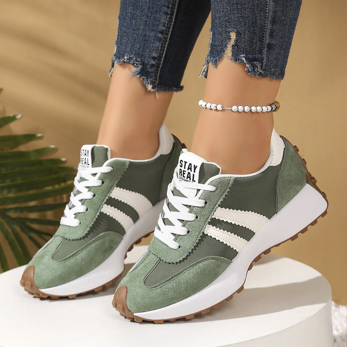 Green and white suede-look lace-up sneakers with thick, chunky soles and white striped accents on a white platform.