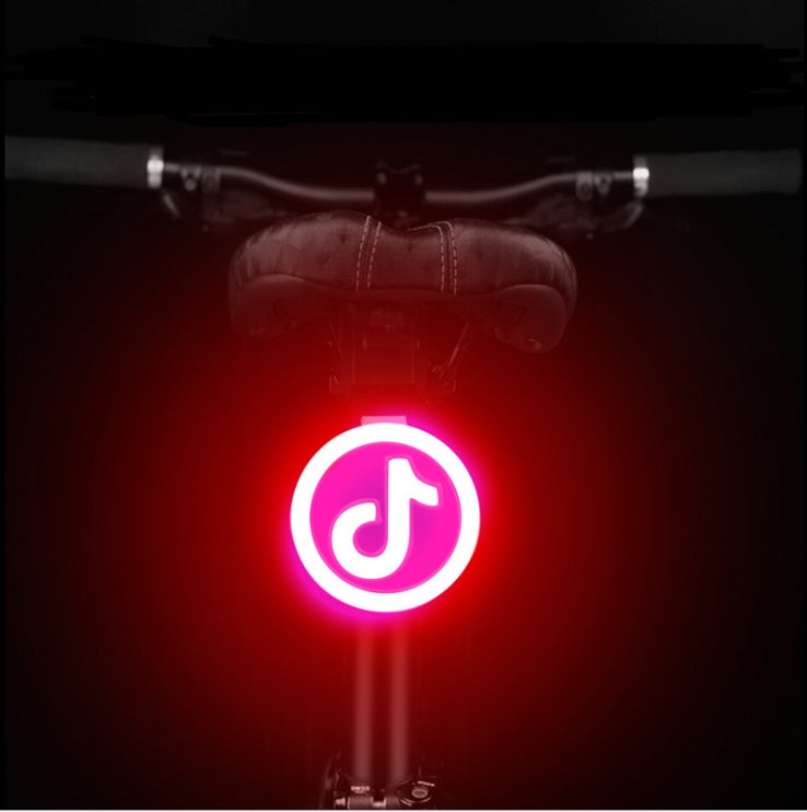A round, red LED bicycle taillight mounted on a bike seat post, glowing with a bright white TikTok logo icon.