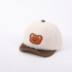 Cream-colored sherpa baby hat with a brown corduroy brim and a cute embroidered bear patch on the front.