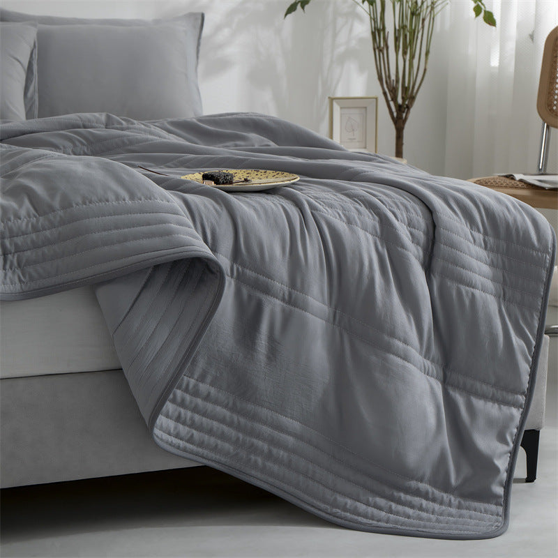 Solid gray summer cooling quilt draped over a bed with horizontal stitching and smooth, lightweight material.