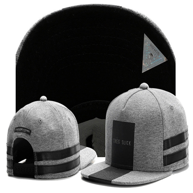 Grey hip-hop snapback hat featuring a black rectangular patch with "TRES SLICK" text and black leather-look stripes.