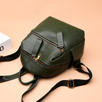 Small olive green top-layer leather backpack with gold zippers, black fabric straps, and a soft pebble-grain texture.