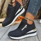 Black perforated athletic sneakers with wedge soles, side zippers, and gold heel accents on a wooden background.