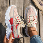 Women’s beige, grey, and red flyknit mesh sneakers with chunky white soles, lace-up fronts, and branded straps.