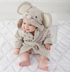 A cute baby wearing a soft, beige cotton hooded bathrobe with mouse ears and a pink nose on a white textured mat.
